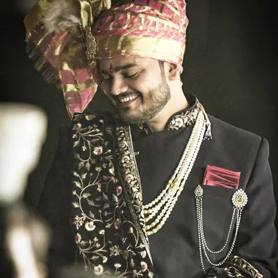 A candid portrait of the groom, capturing his happy and relaxed demeanor. His stylish sherwani, pearl necklace, and embroidered shawl showcase a perfect blend of traditional and modern groom fashion.