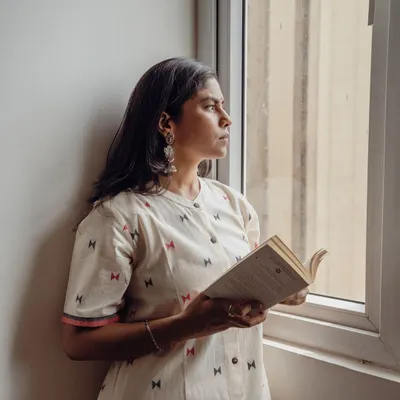 A thoughtful portrait by the window, using soft, natural light to create a serene mood. This shot is part of a lifestyle campaign for an Indian wear brand, perfect for their website or social media.