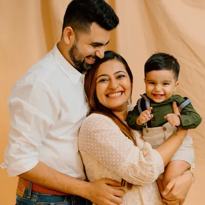This is the essence of a happy family portrait. The warm smiles and loving embrace of this family of three create a timeless and heartwarming image against a simple, neutral backdrop.