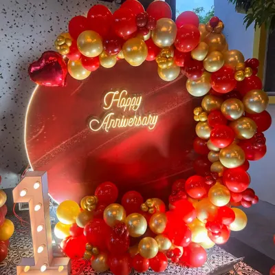 I design bold and beautiful backdrops to celebrate your special milestones. This first-anniversary setup features a vibrant red circular panel, a custom 'Happy Anniversary' neon sign, and a lush garland of red and gold balloons, complete with an illuminated number '1'.