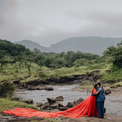 A dramatic pre-wedding portrait with the bride's flowing red dress against a stunning natural landscape. A moment of pure romance and artistry.