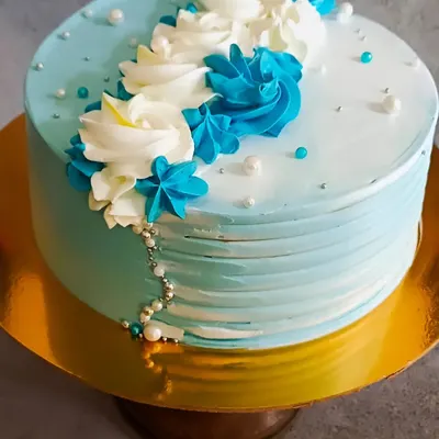 An elegant and simple cake design featuring a beautiful blue and white color palette. The buttercream is textured on the sides and decorated with piped rosettes and delicate sugar pearls.