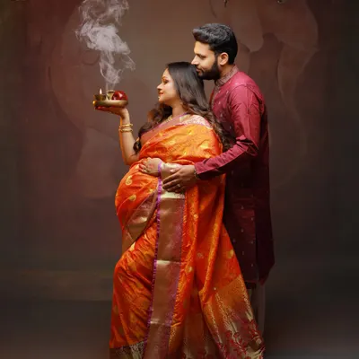 An intimate moment between expecting parents, celebrating their journey with traditional elements like the ceremonial diya. This studio shot combines cultural reverence with artistic lighting.