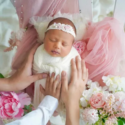 A dreamy portrait of a newborn nestled in a bed of soft pink florals and tulle. This artistic setup creates a magical, fairytale-like image of your sleeping baby.