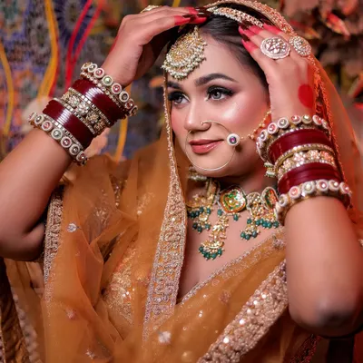A beautiful close-up of a bride in a mustard-gold lehenga, adjusting her dupatta. The red chooda bangles add a pop of traditional color.