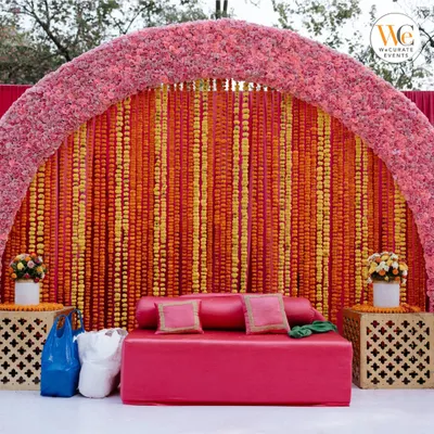 A classic Mehendi seating area is a must. I designed this one with a vibrant backdrop of orange and yellow marigold strings and a comfortable pink sofa for the bride.