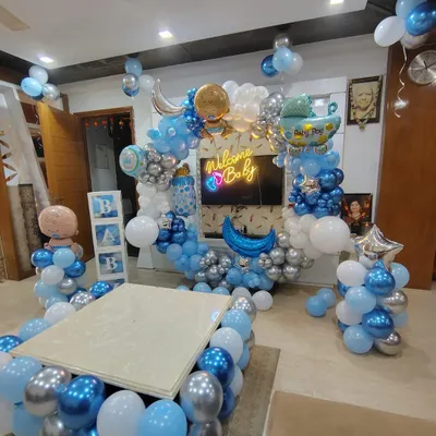 An elaborate welcome home decoration for a baby boy, filling the living room with joy. This setup features a large balloon arch with a "Welcome Baby" neon sign, "BABY" blocks, and balloons surrounding a central table.