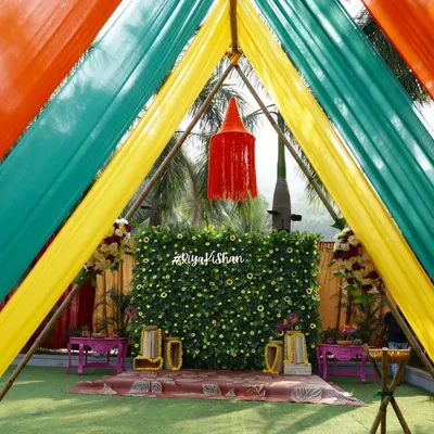 A close-up of our colorful Haldi entrance tunnel. The combination of yellow, green, and orange drapes frames the beautiful floral backdrop, creating a perfect photo opportunity for guests as they arrive.