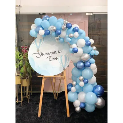 This balloon easel is a beautiful way to welcome guests to Shivansh's first birthday. The "up, up and away" theme on the sign is perfectly matched by the blue, white, and silver balloon garland, creating a cohesive and stylish entrance piece.