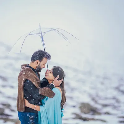 A classic romantic movie moment recreated in the snows of Gulmarg. The couple huddles close under a clear umbrella as snowflakes fall around them, creating a magical and intimate pre-wedding portrait.
