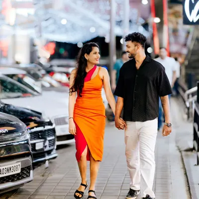 A full-length shot of a couple walking hand-in-hand down a city street at night, with decorative lights creating a beautiful bokeh background.