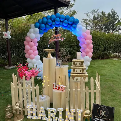 Our decorations are perfect for outdoor settings too. Here, we set up a colorful balloon arch and a personalized display with the name 'HARINI' in marquee letters for a beautiful garden party. The picket fence and props add a charming, rustic feel.