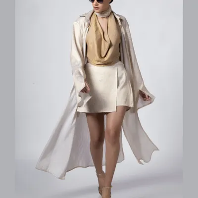 A full-length shot of a model in a flowing beige trench coat and white skirt, walking with confidence. This image captures a sense of movement and high fashion, perfect for an editorial spread or a designer lookbook.