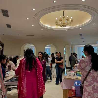 A wide view of the exhibition hall, showing a steady stream of visitors browsing different stalls under the elegant chandeliers of the clubhouse.