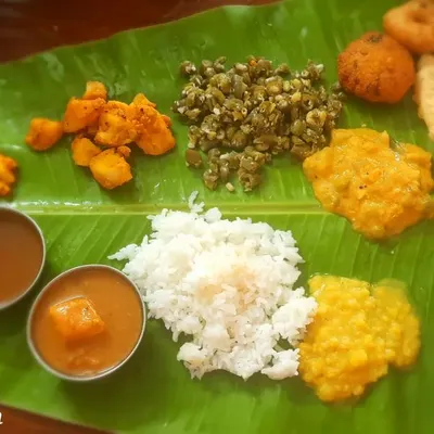 A complete South Indian lunch spread served on a traditional banana leaf. This meal for a housewarming included rice, sambar, rasam, poriyal, vada, and payasam, all made without onion or garlic.