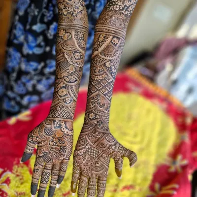 A stunning Dubai-style bridal mehendi that extends to the elbows. The design features a mix of bold floral patterns, intricate netting, and paisley elements.