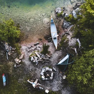 An aerial view of a complete lakeside setup. You can see the tent, the central campfire ring, and a canoe ready for exploration. I choose locations that offer both relaxation and the opportunity for gentle adventure on the water.