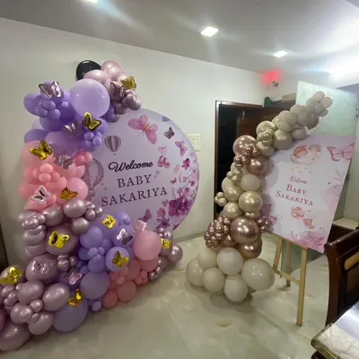 A beautiful butterfly-themed "Welcome Baby" decoration for a home. This setup includes a circular backdrop with custom text, a matching welcome easel, and balloon arrangements in coordinating shades of purple, pink, and rose gold.