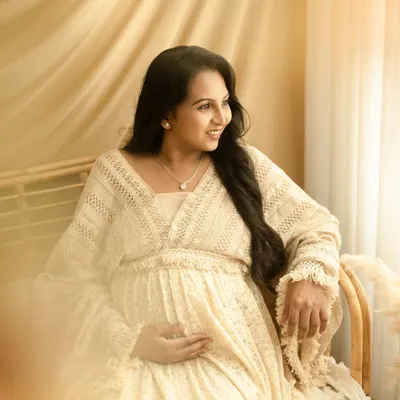 A quiet, contemplative moment for the mom-to-be. The soft, natural window light and boho decor create a peaceful setting for this solo maternity portrait.