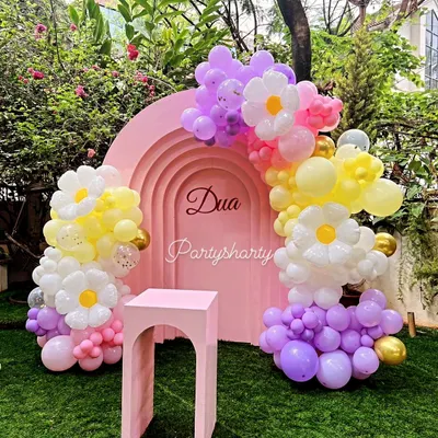 A beautiful outdoor cake cutting setup with a pink arched backdrop and daisy-themed balloon decorations on a lush green lawn.