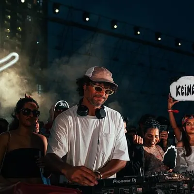 The vibe is everything. Here's &ME of the Keinemusik crew at the decks, with the iconic smiley logo and a fan holding a "Keinemusik" sign. This is the authentic, community-driven atmosphere I cultivate.