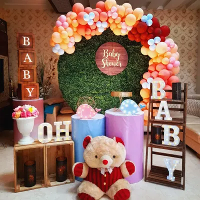 A colorful and fun baby shower setup. This design features a vibrant balloon arch, a green wall backdrop, and playful elements like a teddy bear and "Oh Baby" letter blocks.