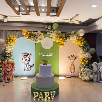 A classic "Wild One" jungle theme for a first birthday, using a three-panel arched backdrop with cute safari animal graphics. The scene is framed by an organic balloon arch in gold and shades of green, with marquee letters for the name.