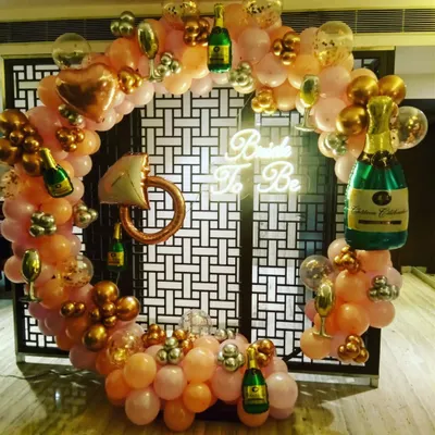 A fun and bubbly "Bride To Be" party setup. This circular balloon arch in pink and gold is decorated with champagne bottle and ring-shaped foil balloons, perfect for a bachelorette party or bridal shower.