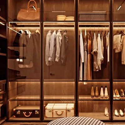 A beautifully styled walk-in closet featuring profile glass doors and warm LED lighting. This design turns your wardrobe into a personal showroom, keeping everything visible and organized.