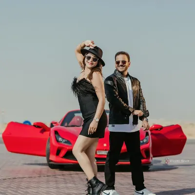A cool, edgy pre-wedding shot in the Dubai desert featuring a vibrant red Ferrari. The couple's leather jackets and confident poses create a powerful, movie-poster look.