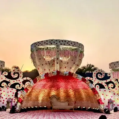 A truly unique reception stage design featuring massive, ornate structures covered in a gradient of red and pink flowers. The central floral dome creates a dramatic focal point for the couple's seating, perfect for a lavish outdoor celebration.