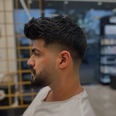 This is a classic example of a mid-fade. Notice the seamless blend from the shorter sides to the longer, textured hair on top, paired with a neatly shaped beard. This is a versatile and popular men's hairstyle.