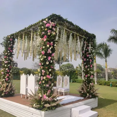 A beautiful floral mandap for an outdoor wedding, with pillars covered in pink and white roses and a canopy of hanging white flowers, creating a classic and romantic look.