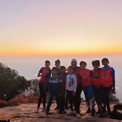 A group of young campers stands together against a beautiful sunrise at Skandgiri. Our camps are designed to inspire a love for nature and create unforgettable moments like this.
