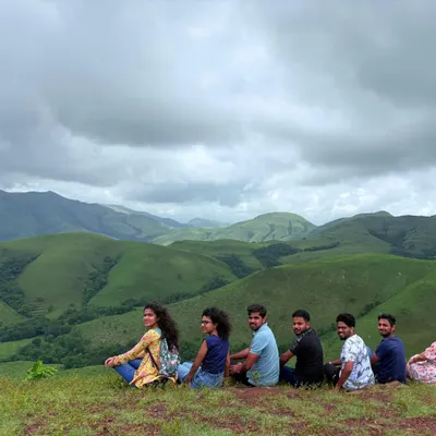 A group of trekkers relaxing and enjoying the spectacular view of the rolling green hills from a viewpoint on the Kudremukha trail.