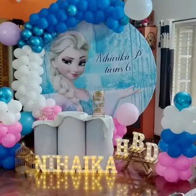 A magical Frozen-themed birthday party for Niharika's 6th birthday. The centerpiece is a large circular backdrop featuring Elsa, framed by a blue, white, and pink balloon arch, perfect for a home celebration.