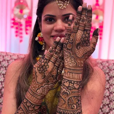 A beautiful bride, adorned with floral jewelry, proudly showing her intricate bridal mehendi. Her happy smile is the best reward for my work.