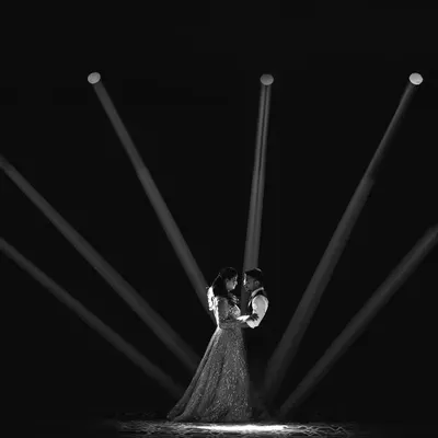 A dramatic black and white photo where the couple is embraced under a fan of spotlights. This high-contrast, artistic shot creates a powerful and cinematic focal point.