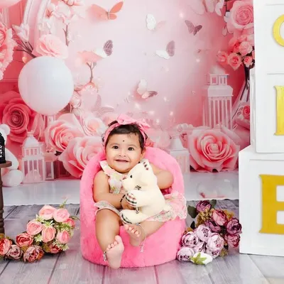A joyful first birthday portrait set against a custom pink floral backdrop. The stacked 'ONE' blocks clearly mark the occasion, while the baby's happy expression is the true centerpiece of the photo.