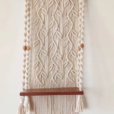 I designed this macrame wall shelf with a beautiful leafy vine pattern as the backdrop. The sturdy wooden shelf is perfect for holding small plants, books, or even creating a small, peaceful mandir space in your home.