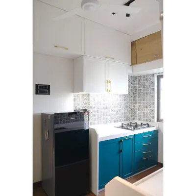 This kitchen for influencers Abhi and Niyu features a beautiful dual-tone design with a rich teal PU finish on the lower cabinets and classic white uppers, complemented by elegant brass handles.