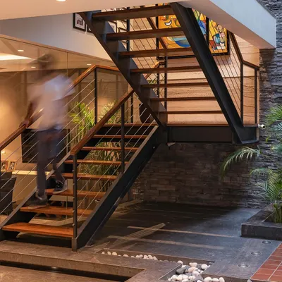 A staircase should be more than just functional; it should be a sculptural element. This design integrates seamlessly with the living space, featuring an indoor court with pebbles and greenery below, bringing light and life into the home's core.