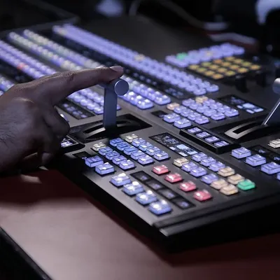 A technician's hand on a professional video switcher demonstrates the complex integration we manage. Our systems allow for smooth transitions between multiple video and audio sources, essential for live events and conferences.