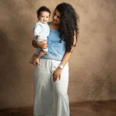 A mother's gentle gaze at her smiling baby. This classic studio portrait, with its warm brown backdrop, beautifully highlights the love and connection between them.