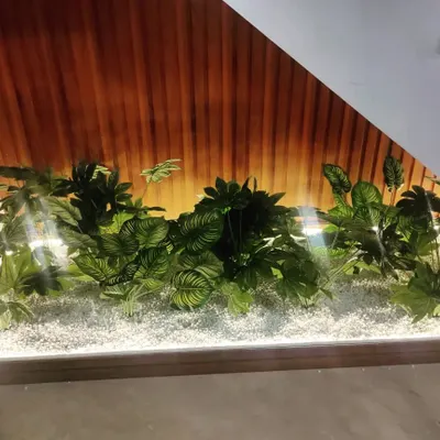 We turned this unused space under a staircase into a beautiful indoor garden. Using a bed of white pebbles and a variety of artificial plants with large leaves, we created a focal point that is both elegant and maintenance-free.