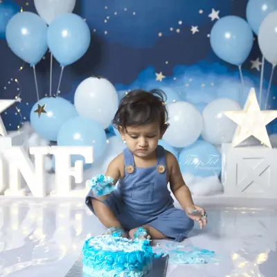 The messy fun of a first birthday cake smash! This little one is digging into a blue frosted cake, set against a dreamy 'twinkle twinkle little star' backdrop.