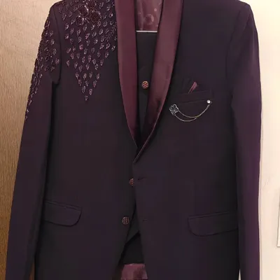 This is a stylish three-piece suit in a deep wine color, available for rent. It features unique shoulder detailing and a matching vest, perfect for making a statement at a wedding or pre-wedding shoot.
