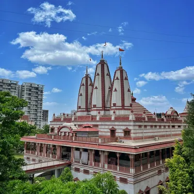 The beautiful white and red shikhara of the ISKCON NVCC temple in Pune, framed by lush green trees and a bright blue sky.