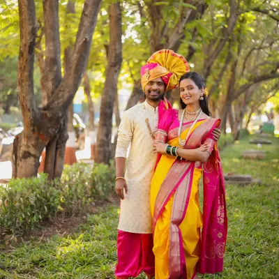 A classic full-length portrait of a couple in traditional Maharashtrian wedding attire. This outdoor photoshoot in a green, tree-lined park provides a perfect, natural backdrop for their vibrant outfits.