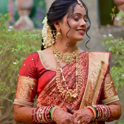 A beautiful South Indian inspired bridal look. The bride is wearing a stunning red and gold silk saree, with traditional temple jewelry and a classic updo adorned with jasmine flowers.